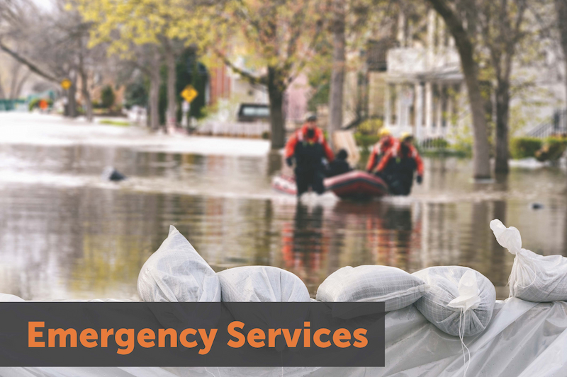 Image: A series of sandbags in the foreground, people in a boat in the background. text: Emergency Services. Links to program homepage.