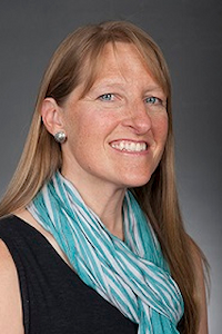 A woman with medium skin tone and blond hair. She is wearing blue pearl earrings, a blue scarf and a black shirt. She is smiling