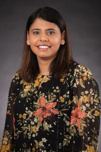 A medium dark skin toned woman with brown hair. She is wearing a black shirt with a floral pattern