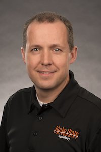 A medium-light skin toned man in a black polo shirt smiling