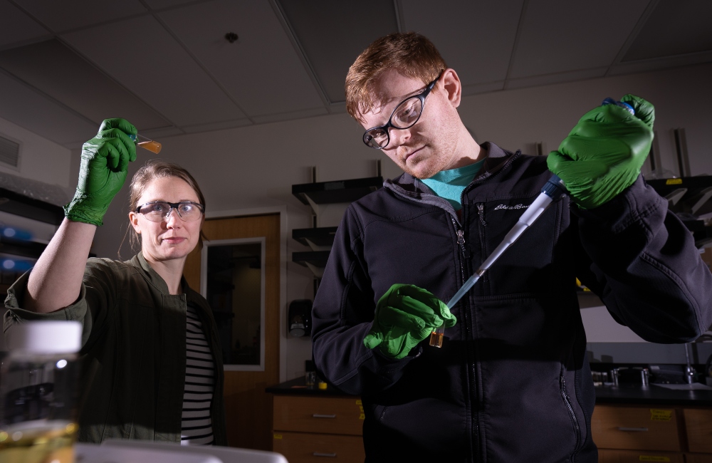 Dr. Cori Jenkins, left, inspects a vial of sulfur-based polymer while Cameron Call prepares a batch of the solution at Idaho State University’s Pocatello campus. Call and Jenkins developed a solution of polymers that captures heavy metals like gold, silver, and lead. This solution can help purify water from industrial waste and test for lead without specialized equipment.