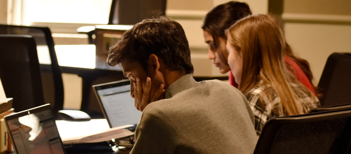 A picture taken from behind 3 students each looking at laptops solving problems