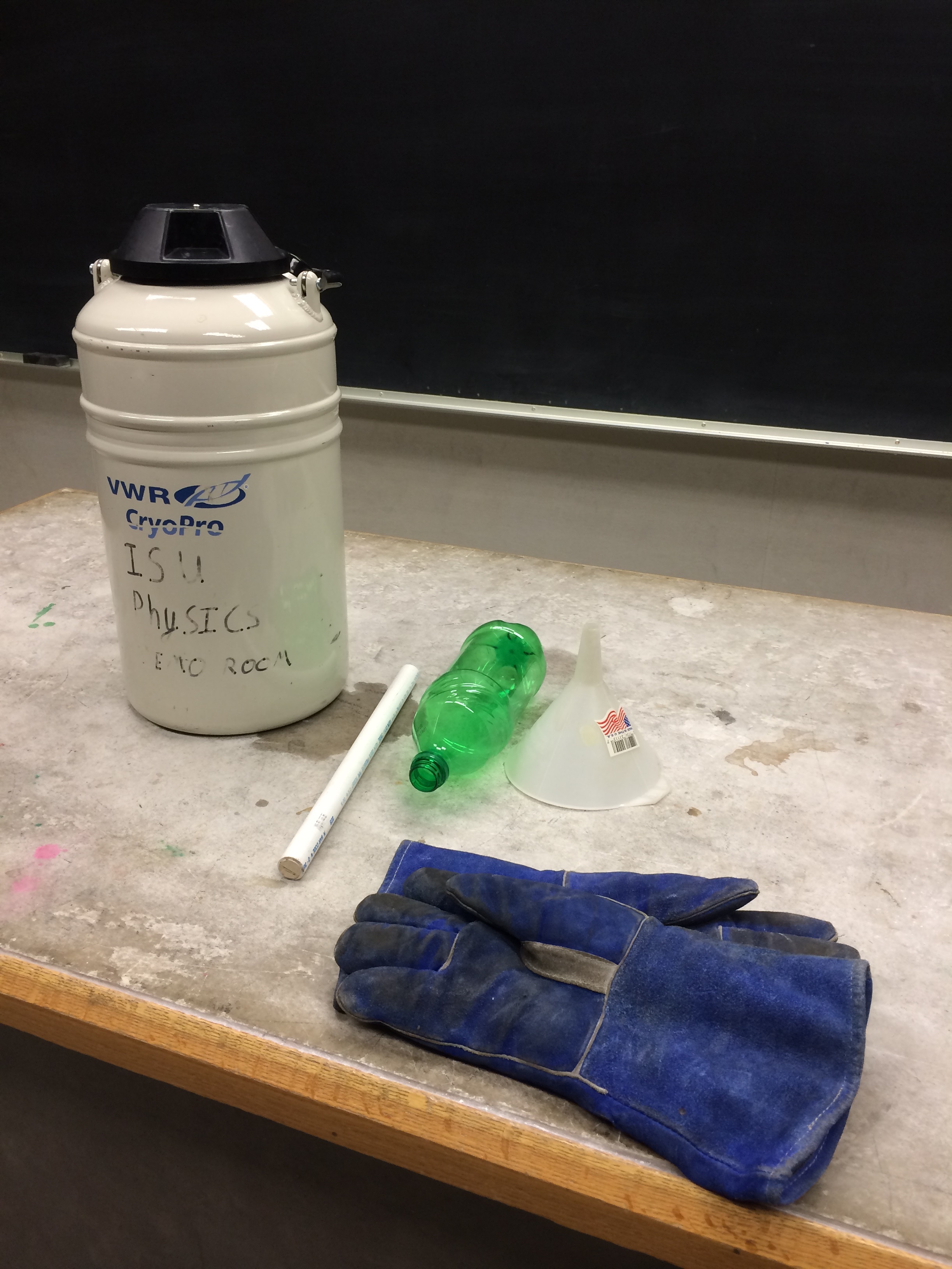 A container of liquid nitrogen by gloves and a small pop bottle