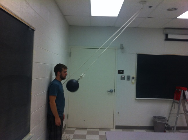 A kid with a bowling ball right next to his nose. The bowling ball is suspended by a line in the air