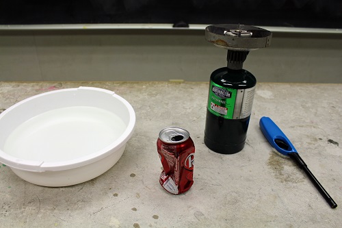 A bowl, pop can, 16 oz propane tank and lighter all on a counter.