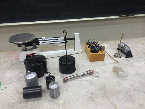 Different Masses between 1 g and 1000g with a triple beam balance scale in the back.