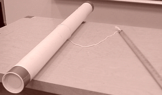 A ruler with a string attached to it with the string wrapped around a tube