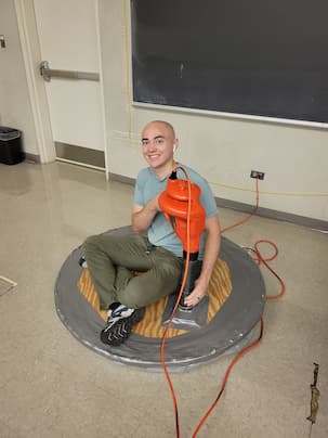 Someone sitting on a piece of wood with a leaf blower inside of the piece of wood and allowing them to float