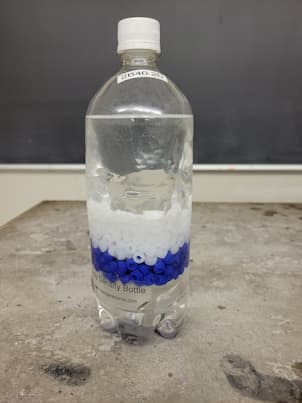 A bottle with white and blue beads in it with alcohol.