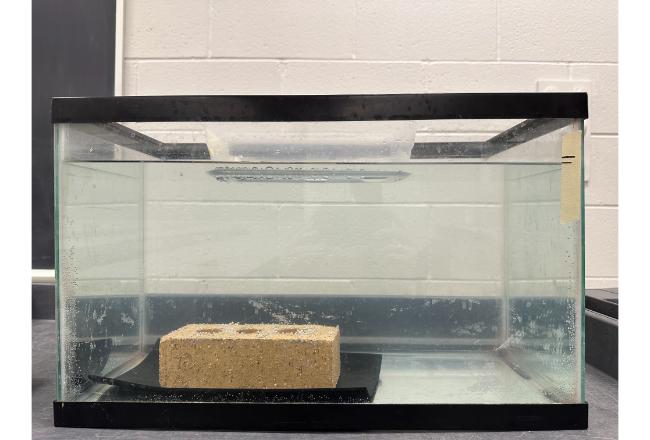 A brick in the bottom of a fish tank, while the tupperware floats at the top. The water level has changed.