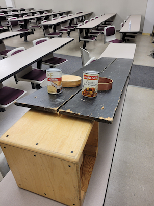 A ramp with soup cans and a wood and steel wheel on it.