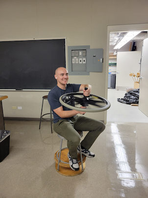 Someone sitting on a stool holing a rotating bicycle wheel