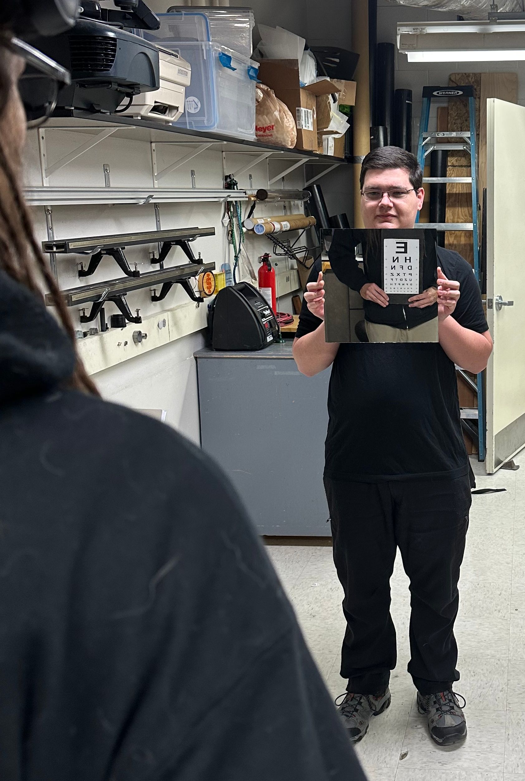 A student holding a mirror with an eye chart in the reflection