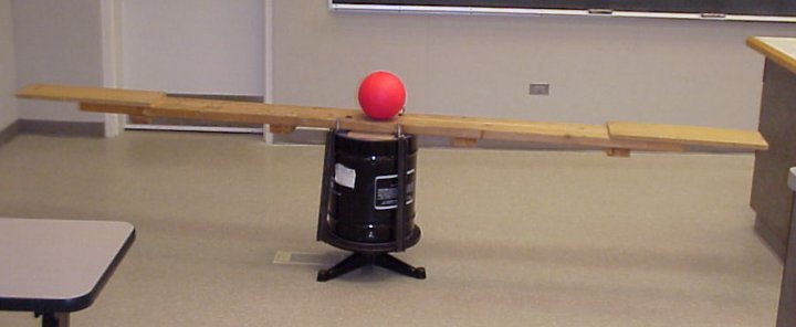 A long 2x4 on a rotating machine with a ball in the middle of the 2x4