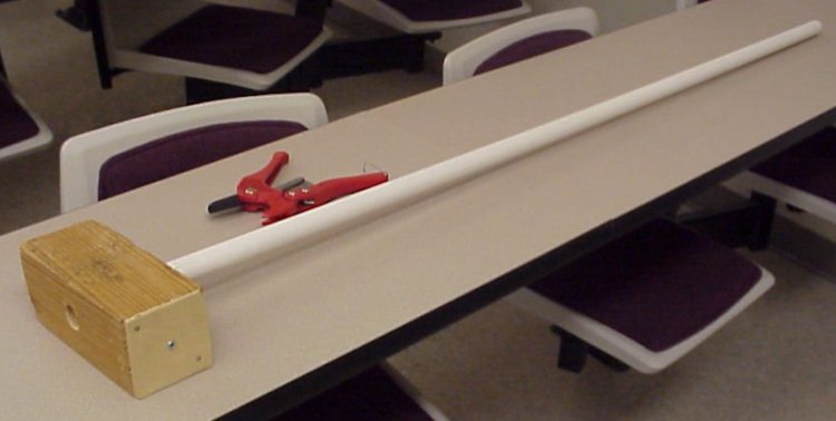 A pvc pipe with a wooden block at the end and pvc pipe cutters laying next to it.