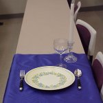 A plate, wine glass, and utensils set up on tablecloth