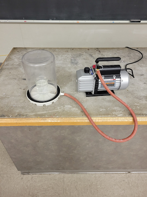a vacuum chamber and pump with a beaker of water inside the chamber
