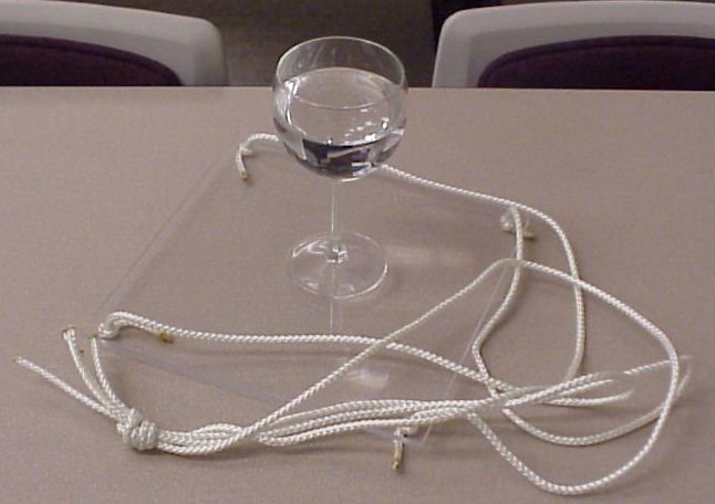 A wine glass on a plexiglass square with ropes attached to the plexiglass