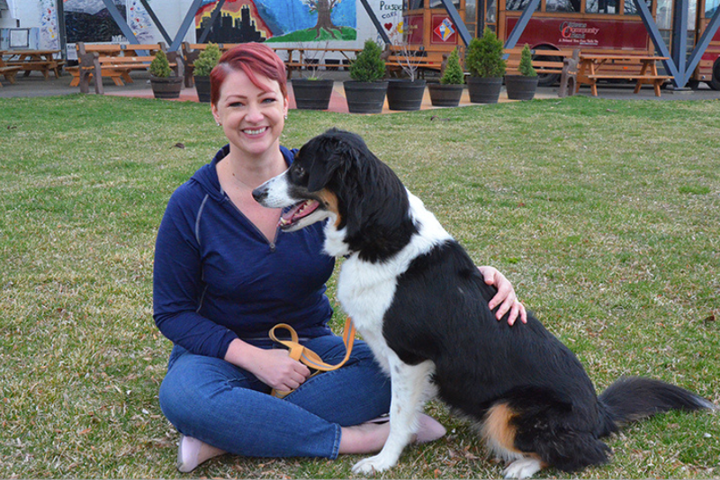 A woman with red hair sitting with her hand on a dog
