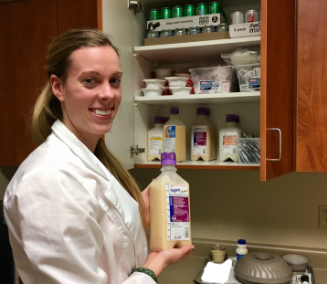 Dietetic intern poses with enteral feeding supplies in hospital supply room