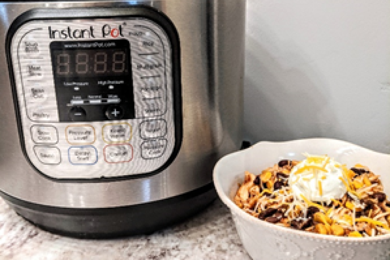 Picture of silver and black Instant Pot, white bowl with food next to it