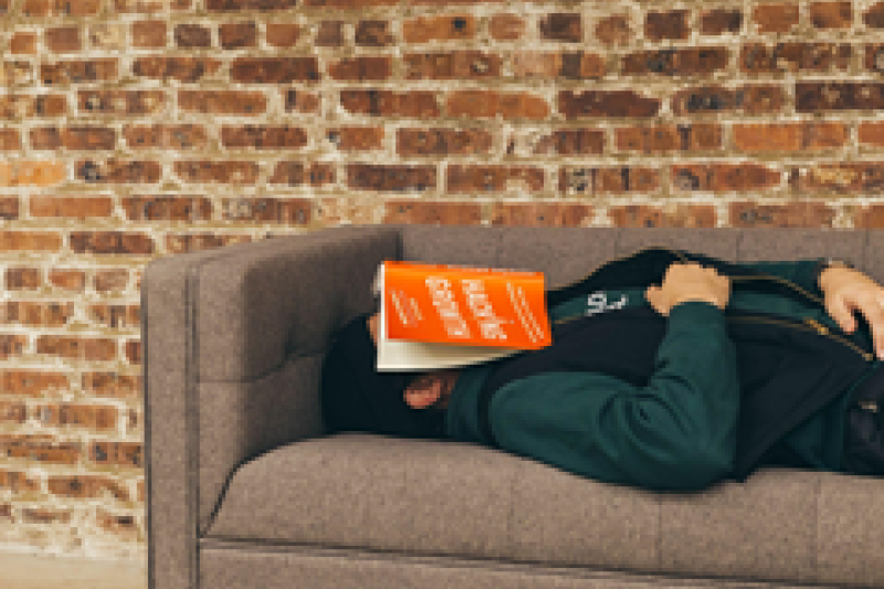 Student sleeping on couch with textbook covering face