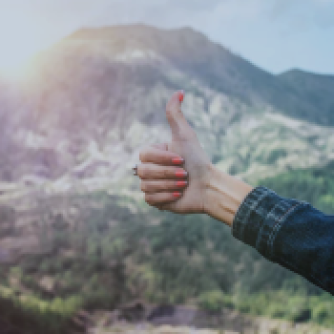 Women holding thumb up with mountains in background