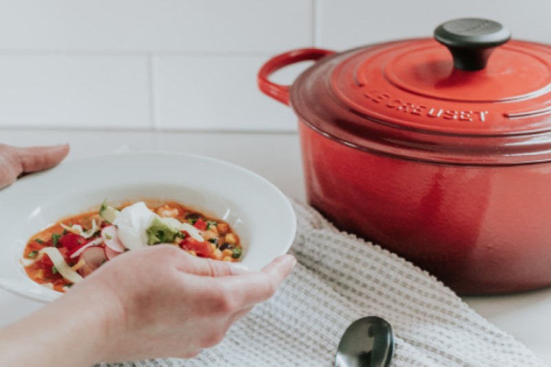 Woman holding bowel of minestrone soup, red pot in background