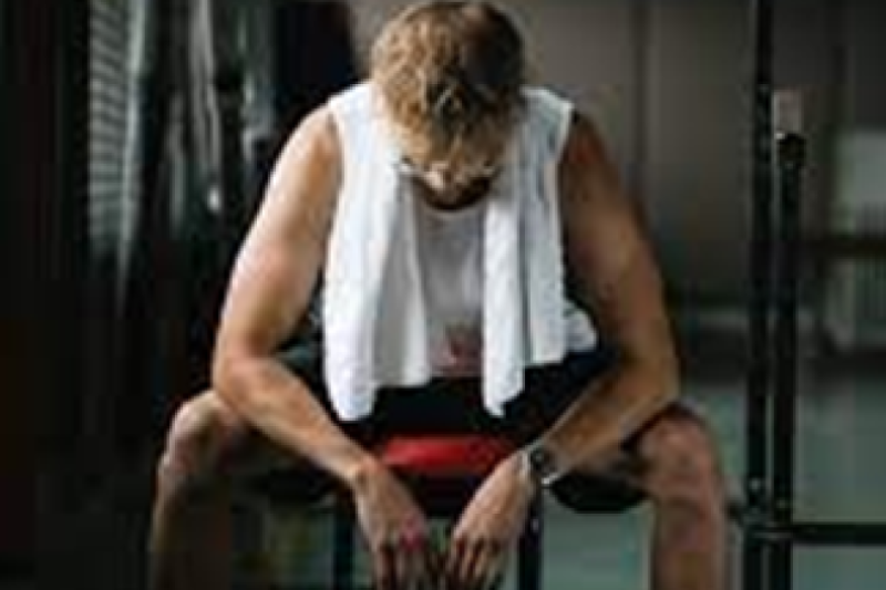 White male sitting on weight bench with towel around neck looking down at floor
