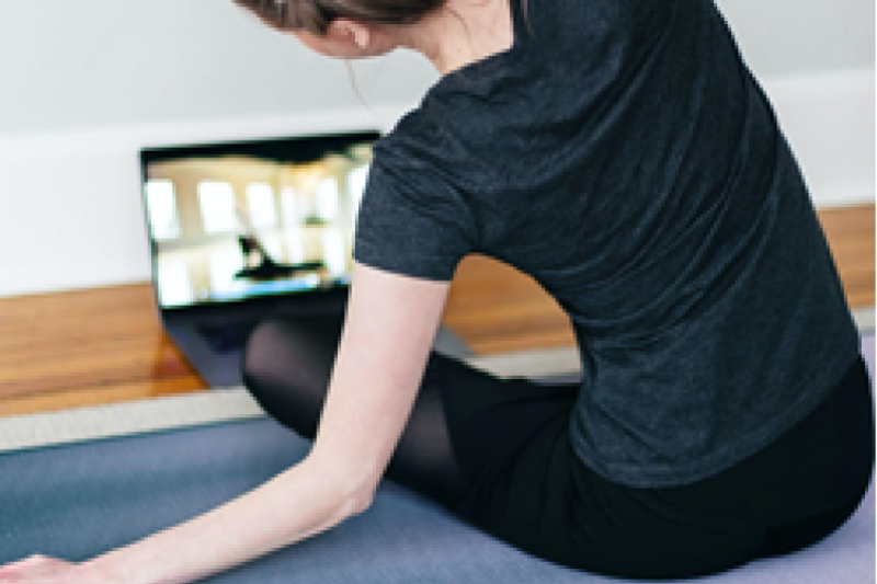 Woman sitting on floor in front of computer, doing stretching exercises