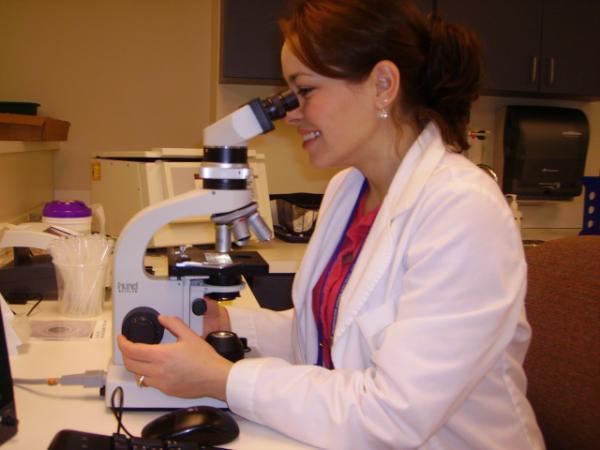 Kami McGann in a white coat using microscope in a lab