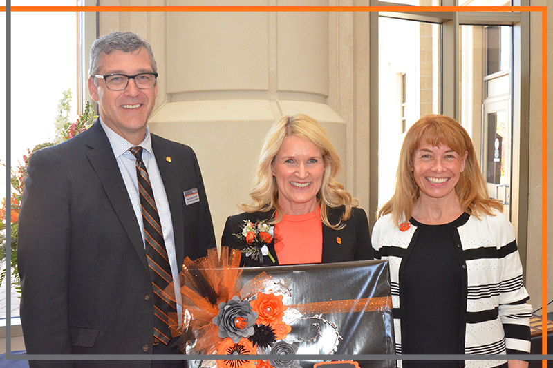 Heidi Halverson holds a plaque decorated with orange and gray paper flowers, with Dr. Rex Force