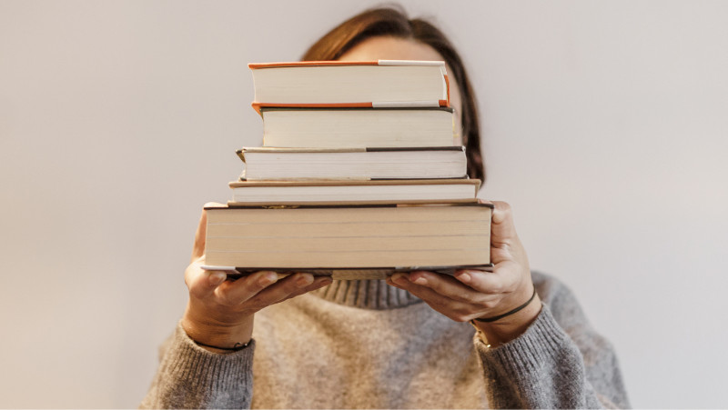 person holding a stack of books in front of their face