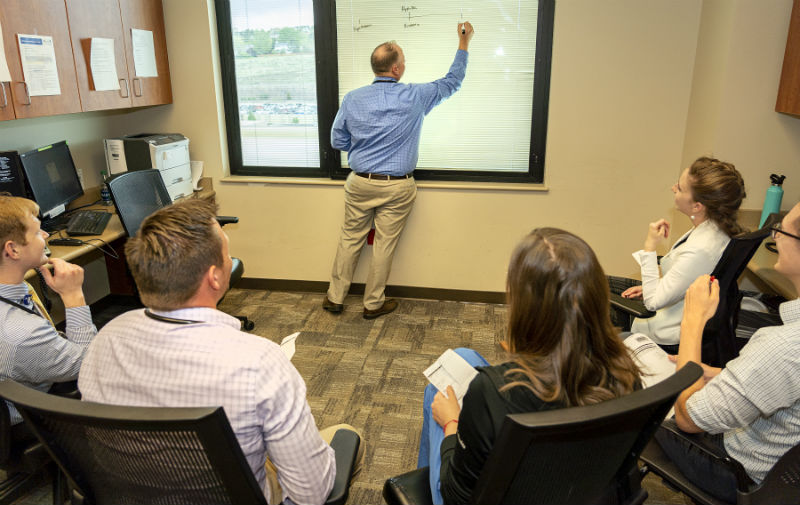 Faculty teaching a group of residents at rounds, writing on board