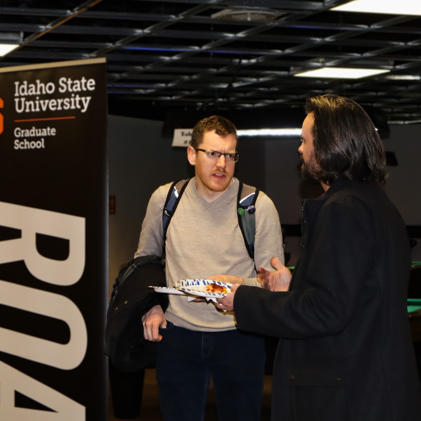 Two graduate students conversing in front of a graduate school banner