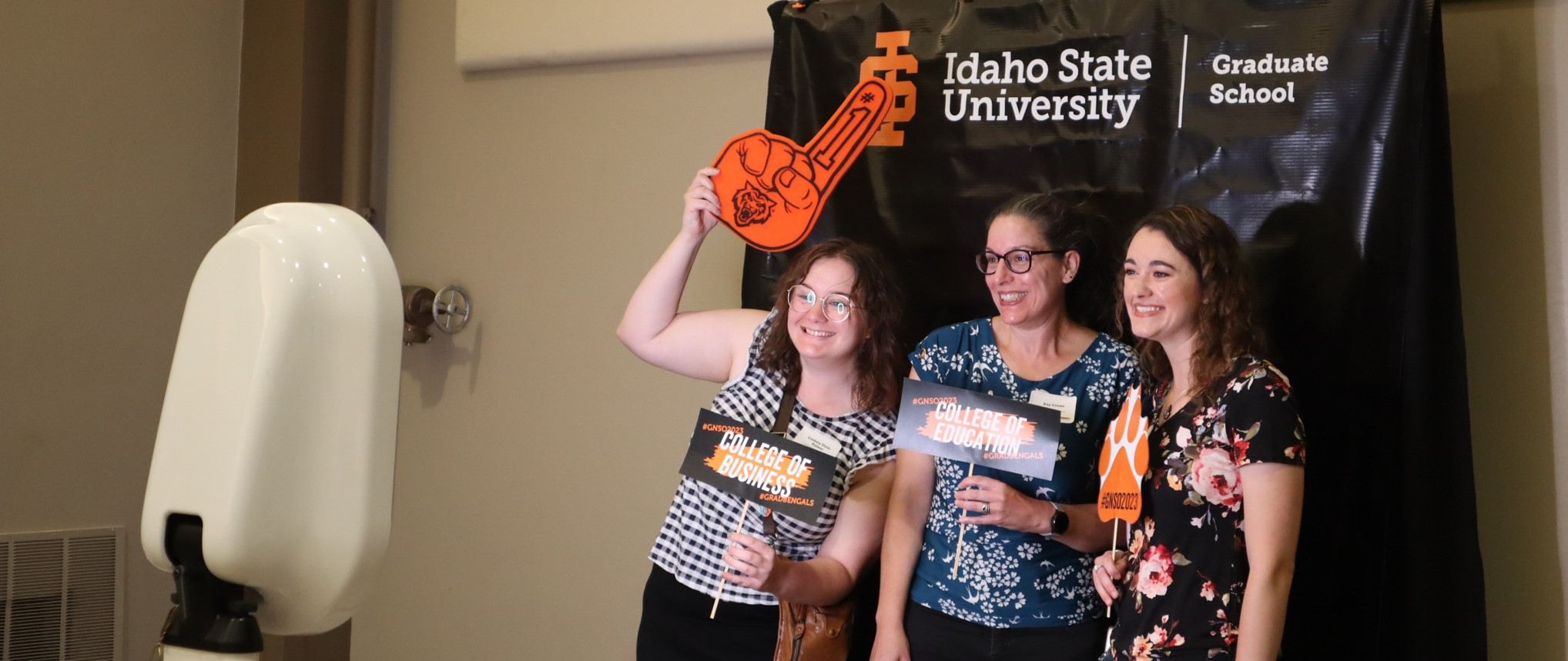 Three students holding up props and taking a photo at the photobooth