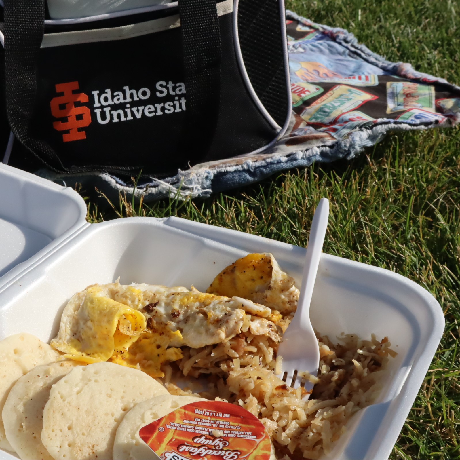 pancakes, eggs, and hashbrowns from the Busy Bee Food Truck in a Styrofoam container near a picnic blanket