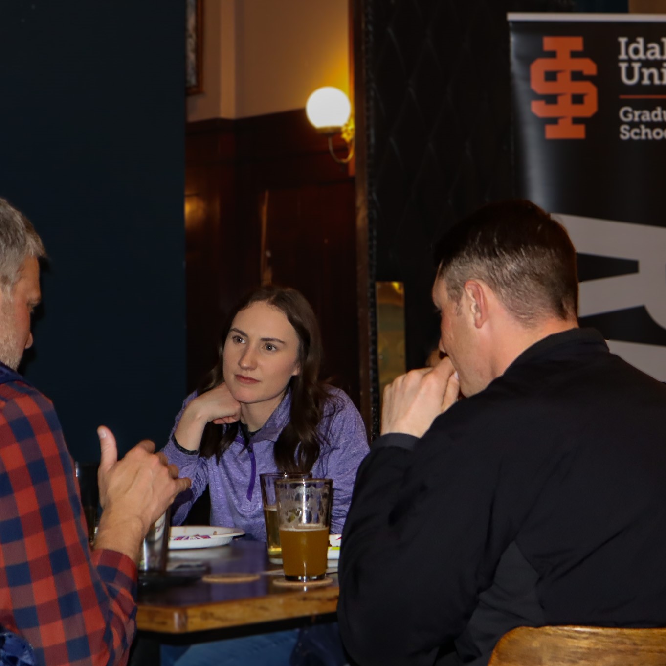 two grad students chatting with a faculty member at a table at late nights