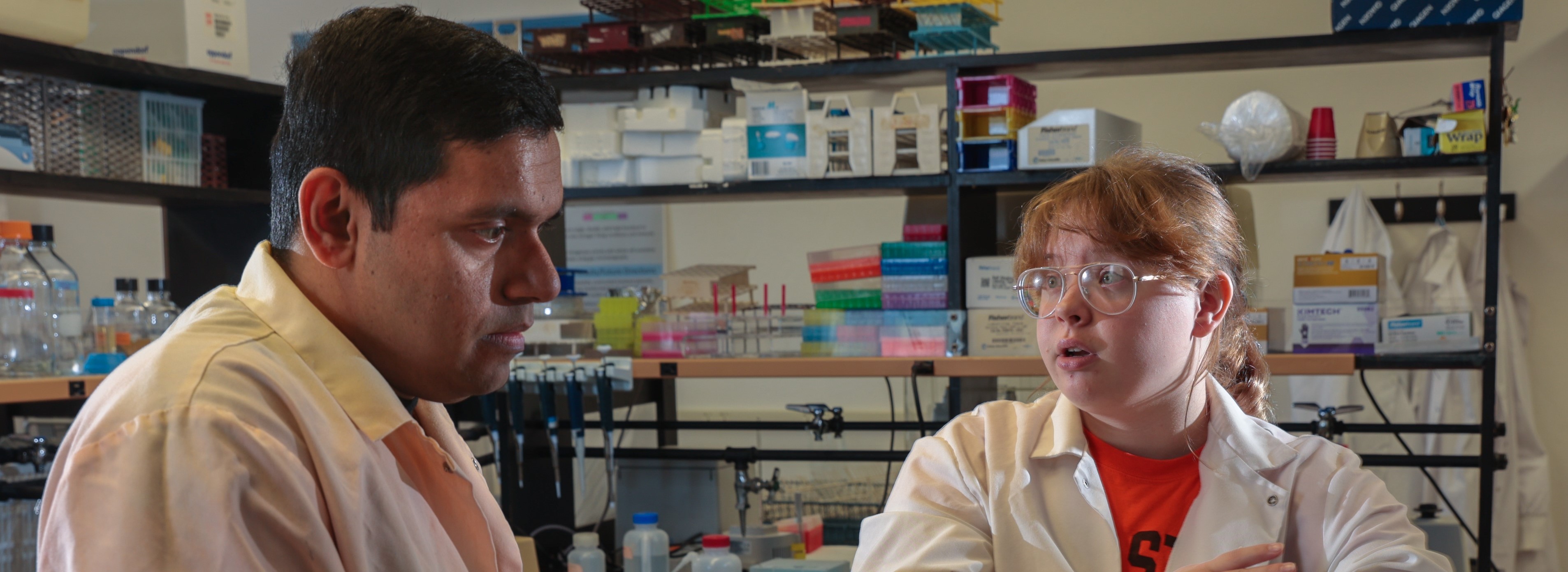 A student and advisor, both in lab coats, conversing