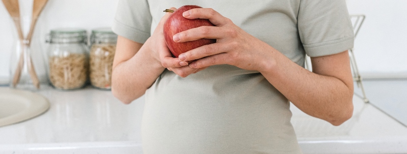 A pregnant woman holding an apple.