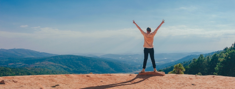 Man standing on a mountain overlook with arms in the air