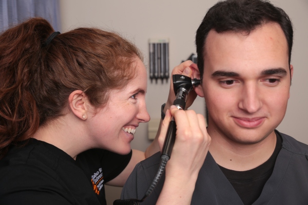 A physician assistant studies student looking into the ear of a patient