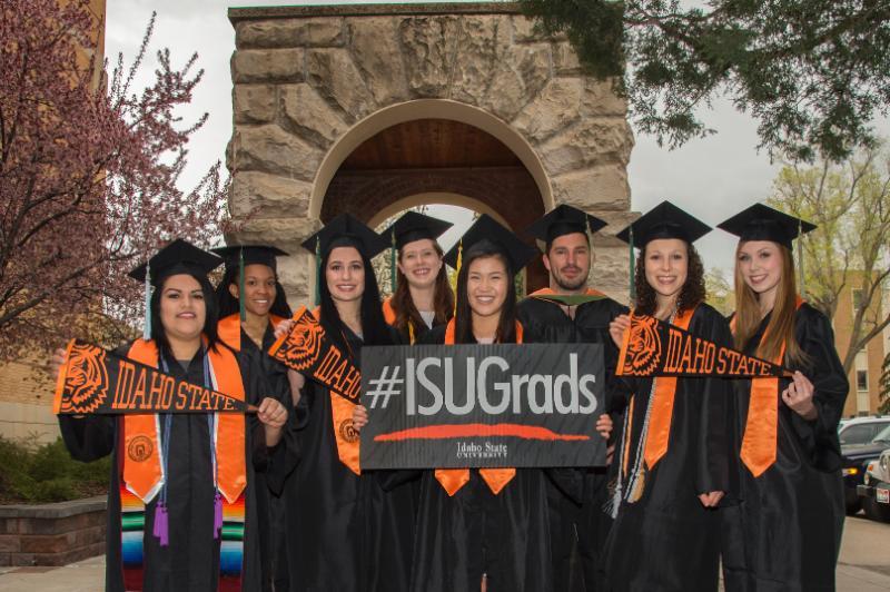 group of ISU graduates in caps and gowns with sign that reads #isugrads