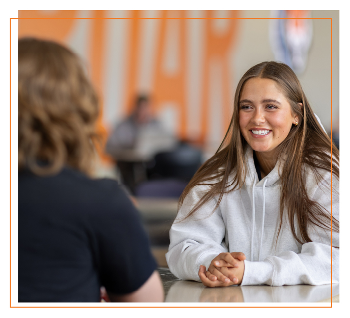 Student smiling while meeting one-on-one with an academic advisor at a table, discussing program options and learning formats at Idaho State University.