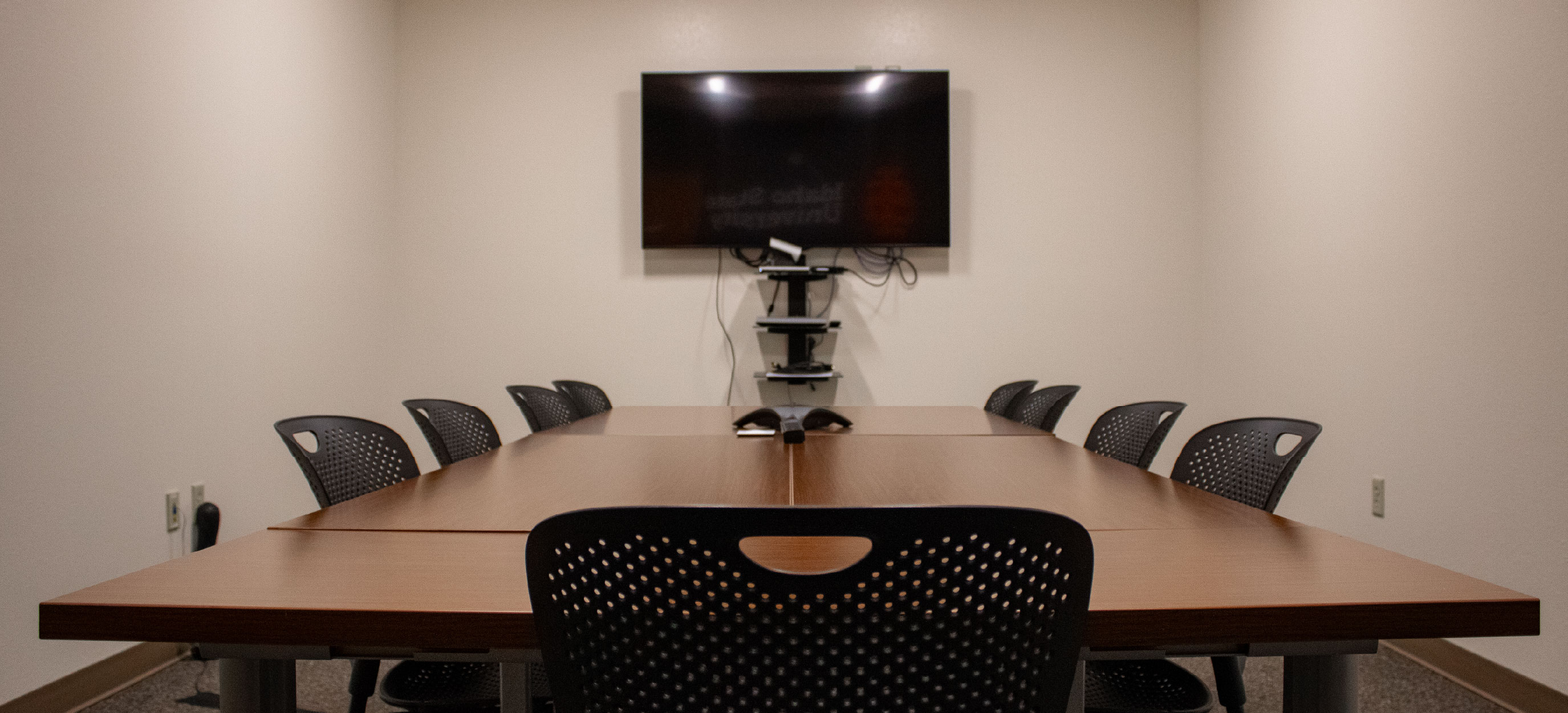 TAB 279 conference room with a large wooden table, black chairs, a conference phone, and a wall-mounted display screen at the front of the room.