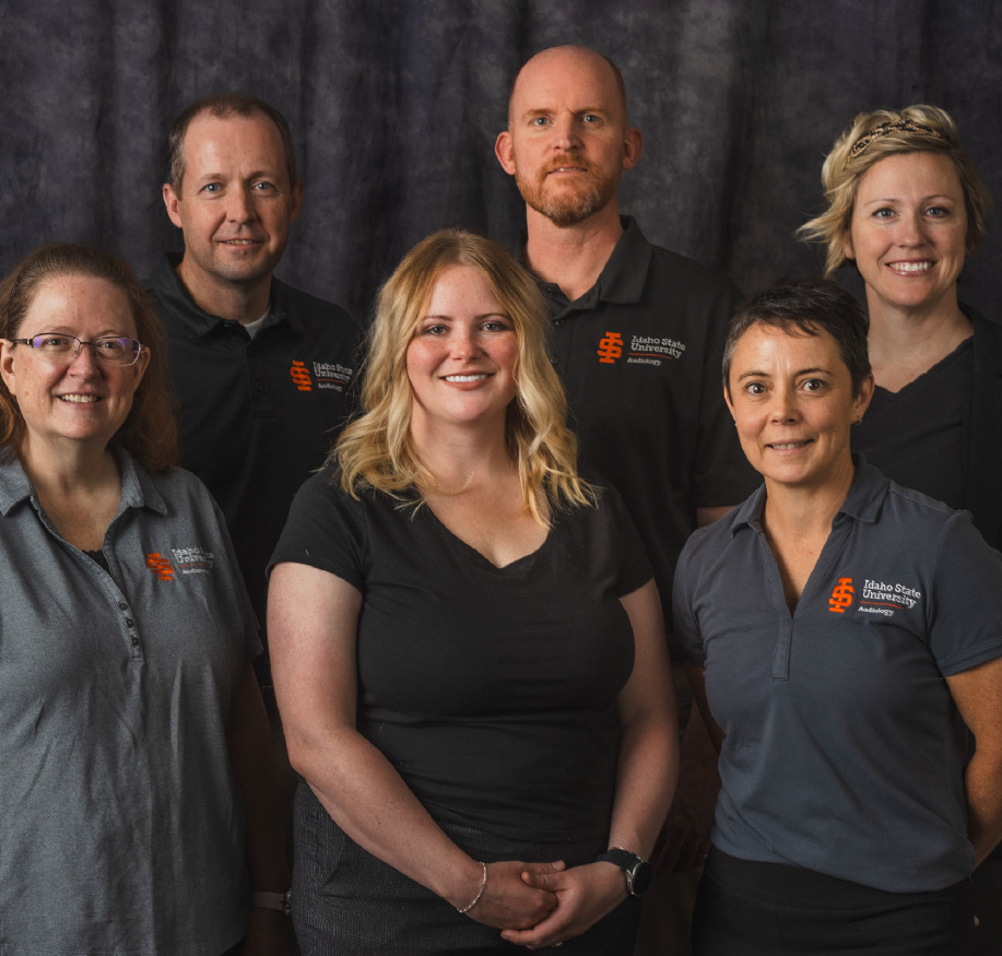 Group portrait of Idaho State University faculty and staff wearing ISU-branded shirts, standing together in front of a dark backdrop.