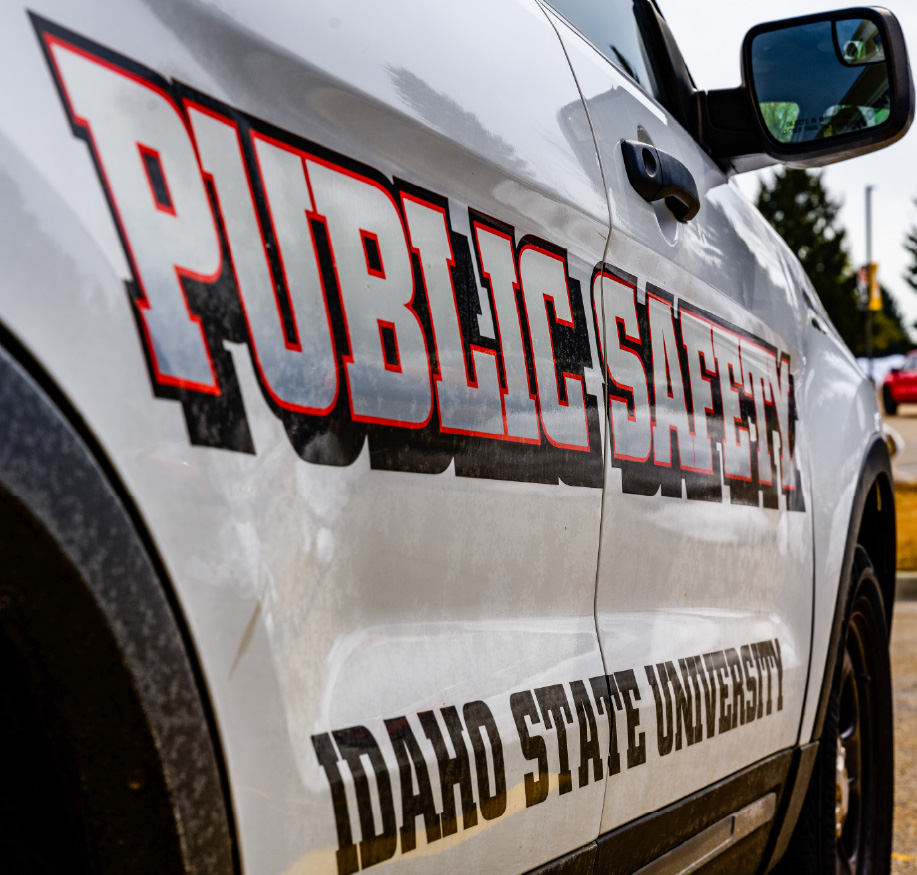Close-up of a white Idaho State University public safety vehicle with bold “PUBLIC SAFETY” lettering on the side door parked on campus.