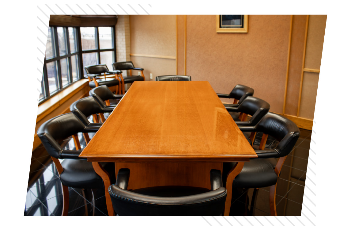 A conference room with a large wooden table surrounded by black leather chairs, with windows along one wall.