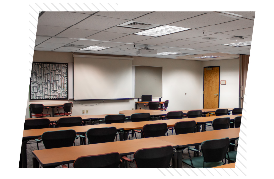 Classroom with rows of tables and chairs facing a projection screen, whiteboard, and instructor workstation at the front of BSUB 109.