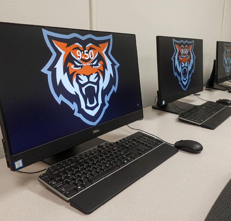 Gemini said A row of Dell desktop computers in a campus computer lab. Each monitor displays the Idaho State University Bengal tiger mascot as the lock screen wallpaper. The time on the screens shows 9:50 AM on Tuesday, March 10. Each station is equipped with a black keyboard and mouse on a light-colored desk.